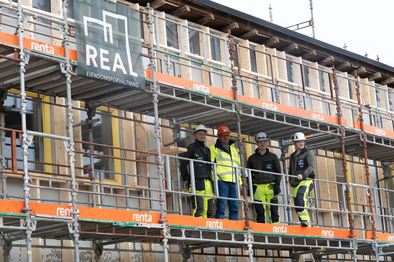 REAL-håndverkere på stillas foran et nybygg